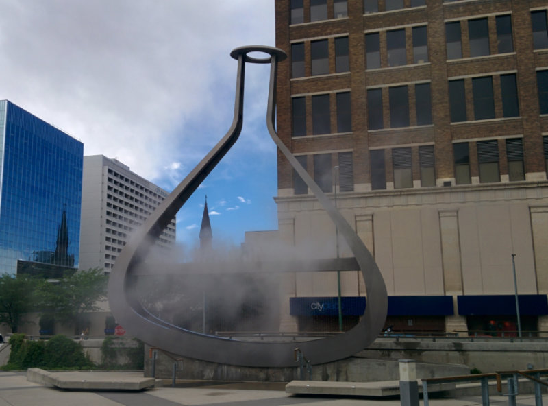 beaker-shaped emptyful statue made of stainless steel, lights, water and fog in Winnipeg, Manitoba