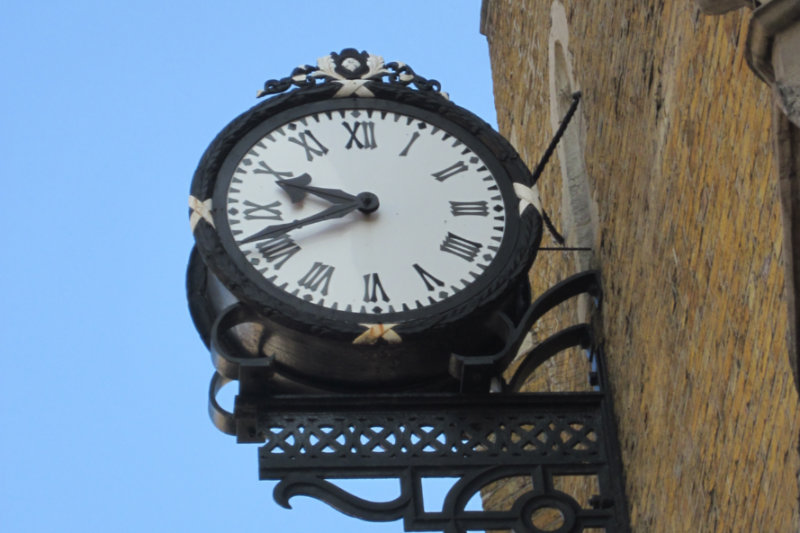 Black metal rimmed clock on the outside of an old stone building