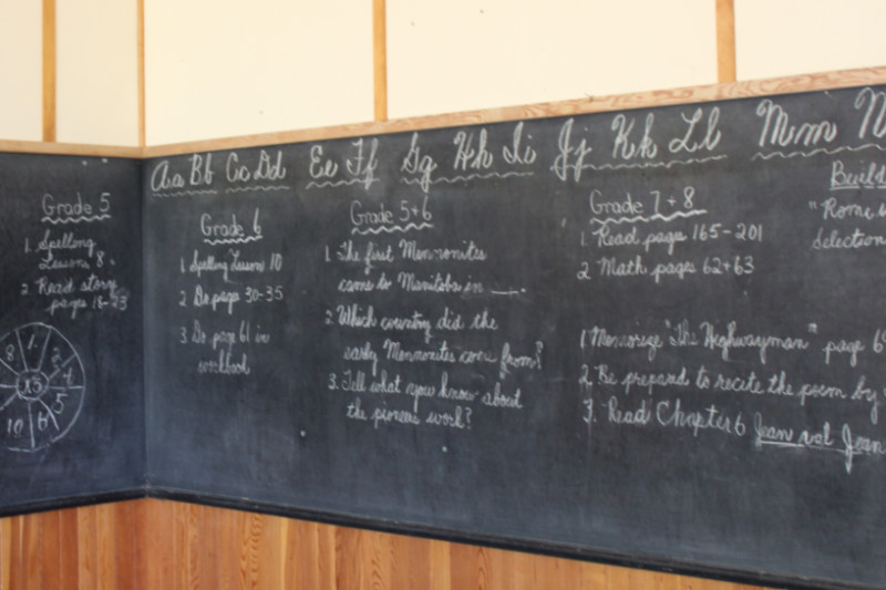 Chalkboard in schoolroom with letters and assignments written in white chalk on it