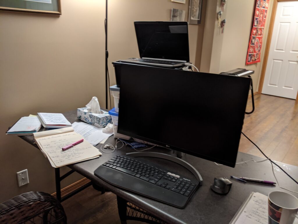 A computer monitor on a long desk with papers and notes spread out around it