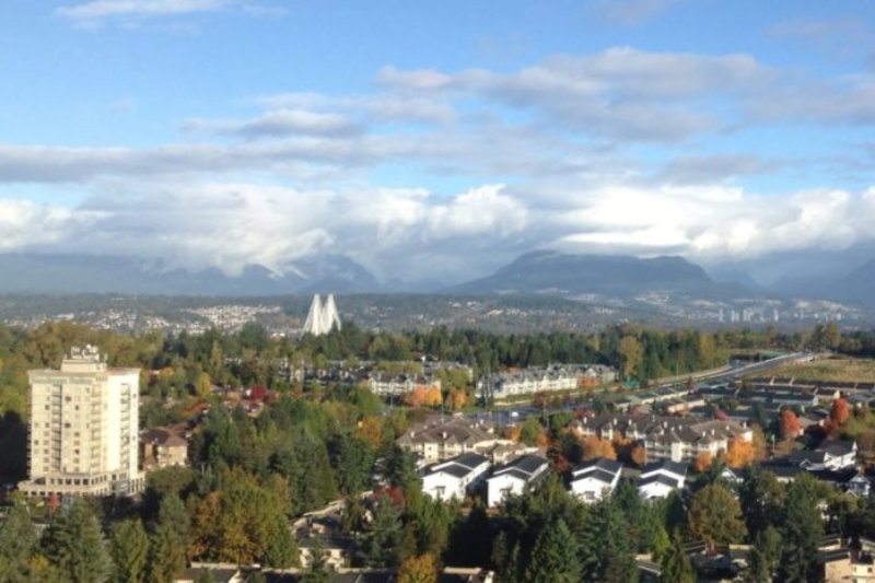 View front hotel window of city among trees with mountain and low-lying clouds in the background