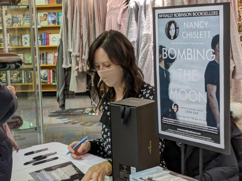 Nancy Chislett at a table signing copies of her book Bombing The Moon
