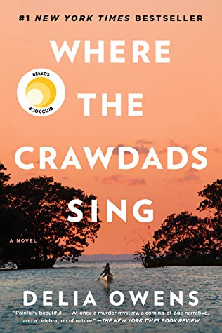 The book cover of Where The Crawdads Sings shows an orangish sky covering the top two-thirds of the page with a grayish-blue lake on the bottom flanked by trees and a figure in a canoe rowing away from us